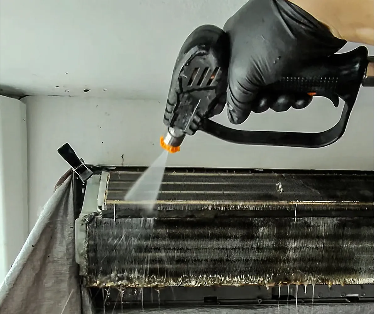 Técnico limpiando con agua a presión el serpentín de un aire acondicionado de pared